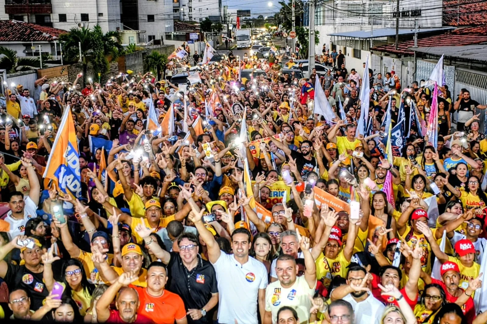 Lucas Ribeiro ergue o braço com a mão em gesto de campanha cercado por multidão em rua do bairro Cristo Redentor.