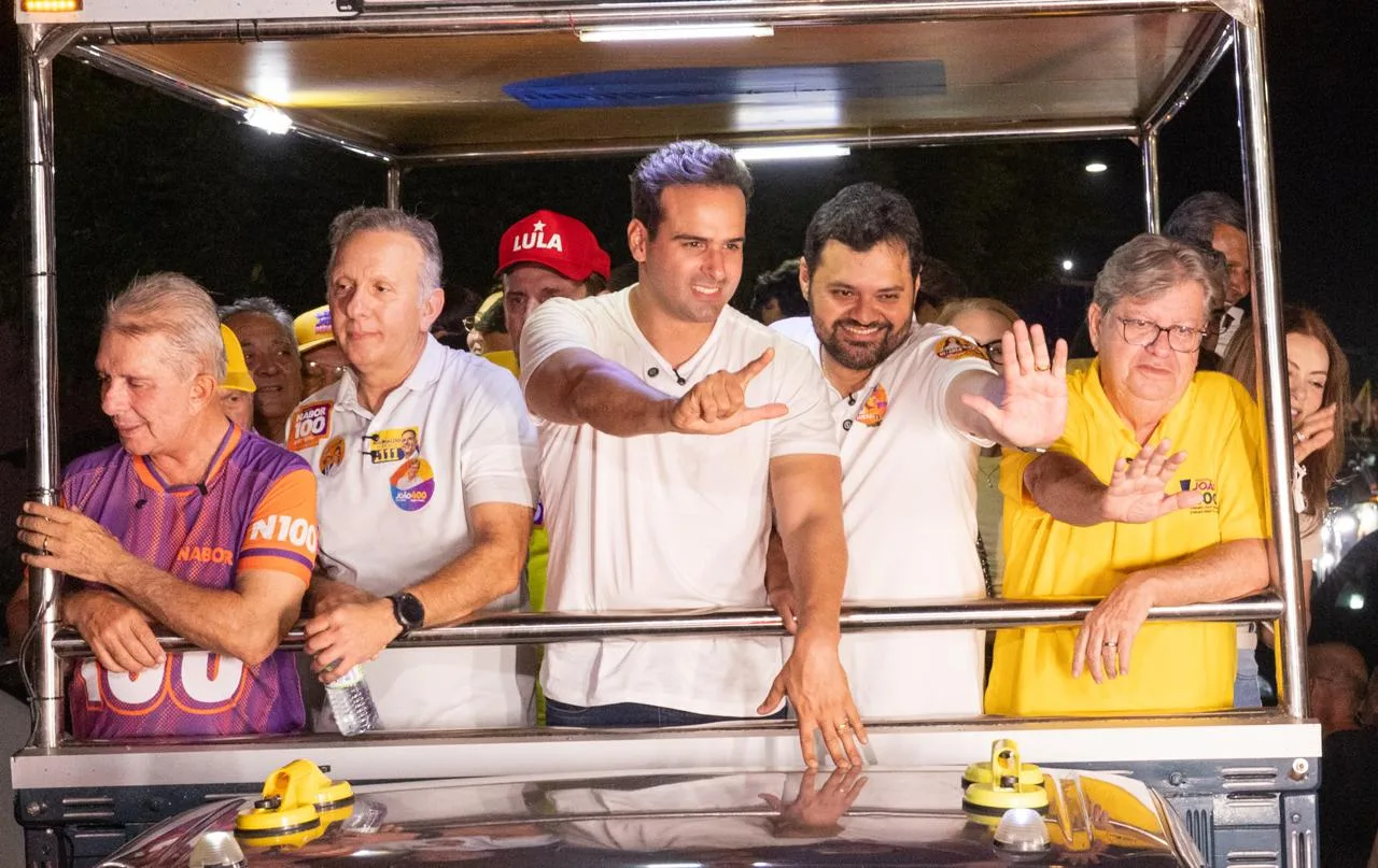 Lucas Ribeiro faz gesto de campanha ao lado de Aguinaldo Ribeiro, João Azevêdo e lideranças em veículo aberto.