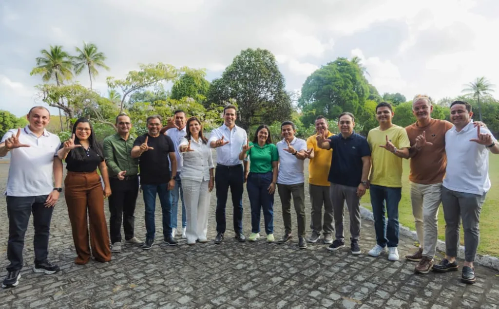 Lucas Ribeiro, Lígia Feliciano, Jackson Alvino, Fernanda Alvino e vereadores de Santa Rita posam alinhados fazendo sinal do 'L' com as mãos em área externa.